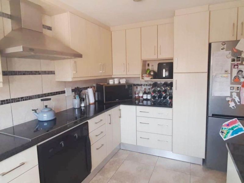 A functional kitchen featuring light-toned cabinetry, dark granite countertops, a built-in oven, electric hob, and a stainless steel extractor fan.
