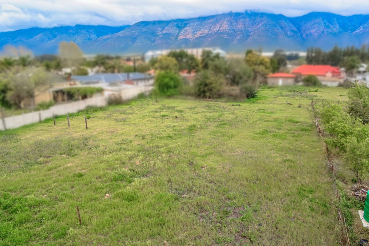An elevated view of a vacant residential plot featuring natural grassland, perimeter fencing, and scenic mountain views in the background.