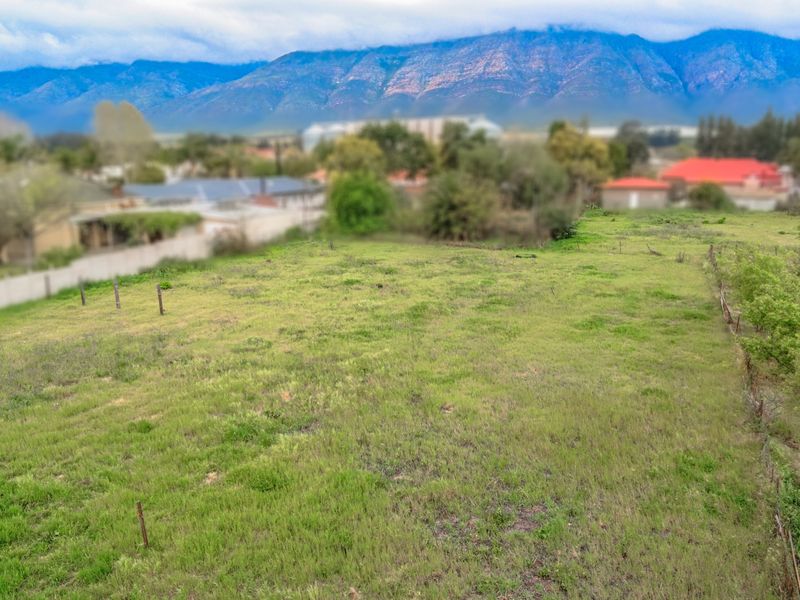 An elevated view of a vacant residential plot featuring natural grassland, perimeter fencing, and scenic mountain views in the background.