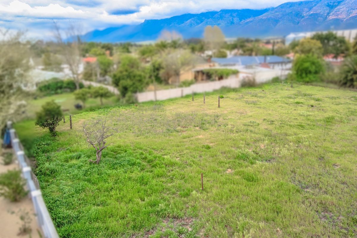 An elevated view of a vacant residential plot featuring grassy terrain and boundary markers, set against a scenic mountain backdrop.