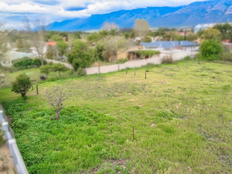 An elevated view of a vacant residential plot featuring grassy terrain and boundary markers, set against a scenic mountain backdrop.