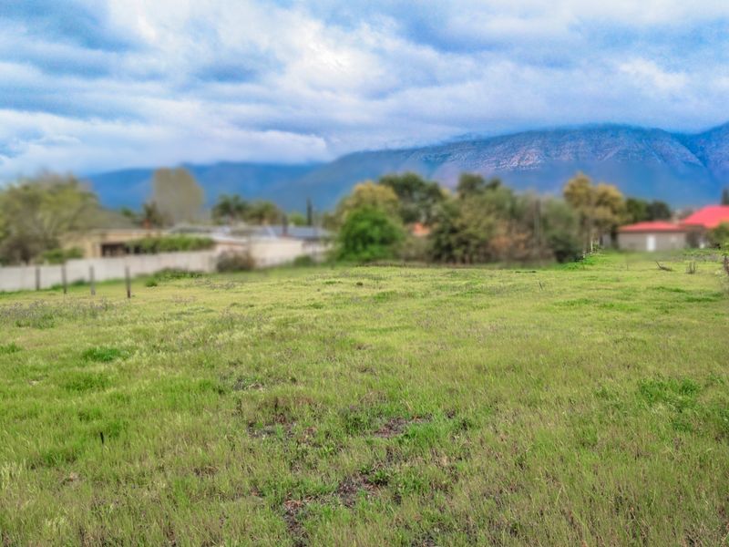 A vacant residential plot featuring grassy terrain with mountain views in the background, suitable for future development.