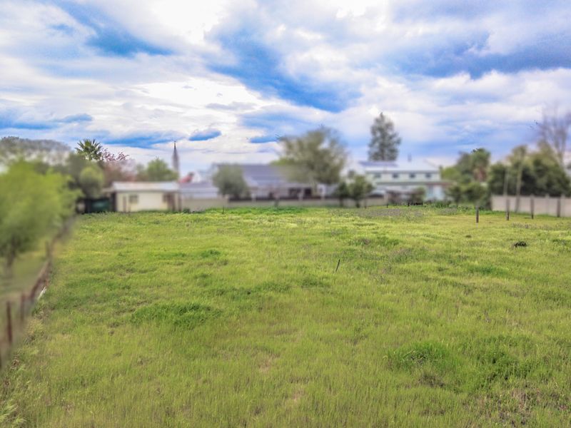 A vacant residential plot of land featuring open grass and perimeter fencing, suitable for future development.