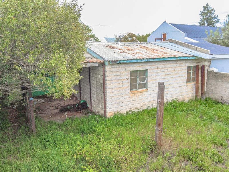 A view of a small, weathered outbuilding on the property featuring masonry block walls and a rusted corrugated metal roof.