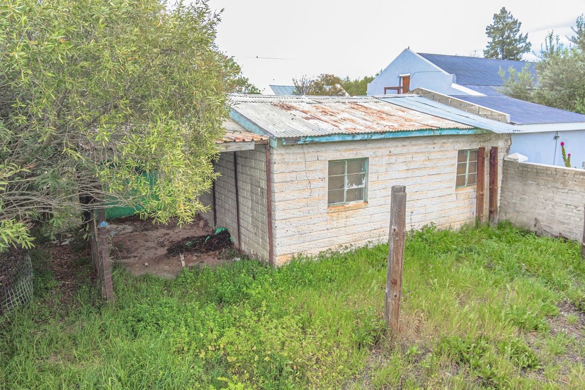 A view of a small, weathered outbuilding on the property featuring masonry block walls and a rusted corrugated metal roof.