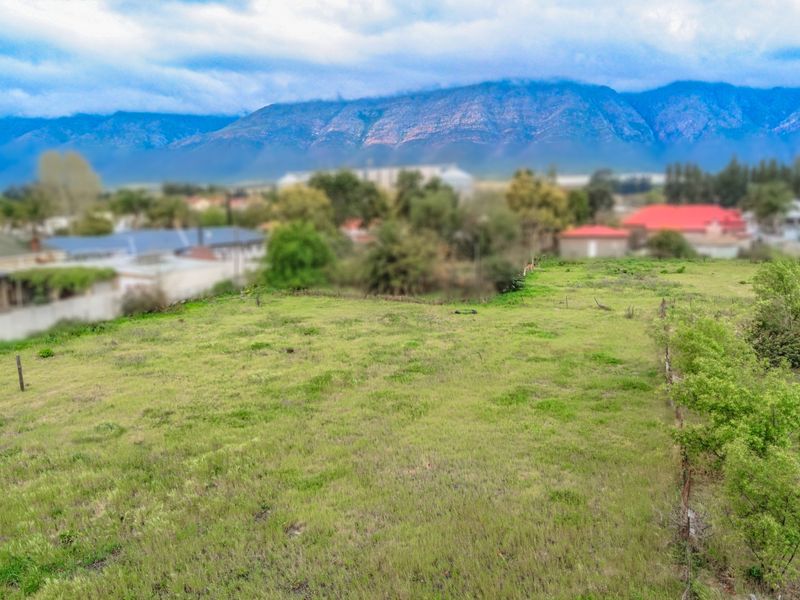 A vacant residential plot featuring natural grass coverage and perimeter fencing, offering scenic mountain views in the background.