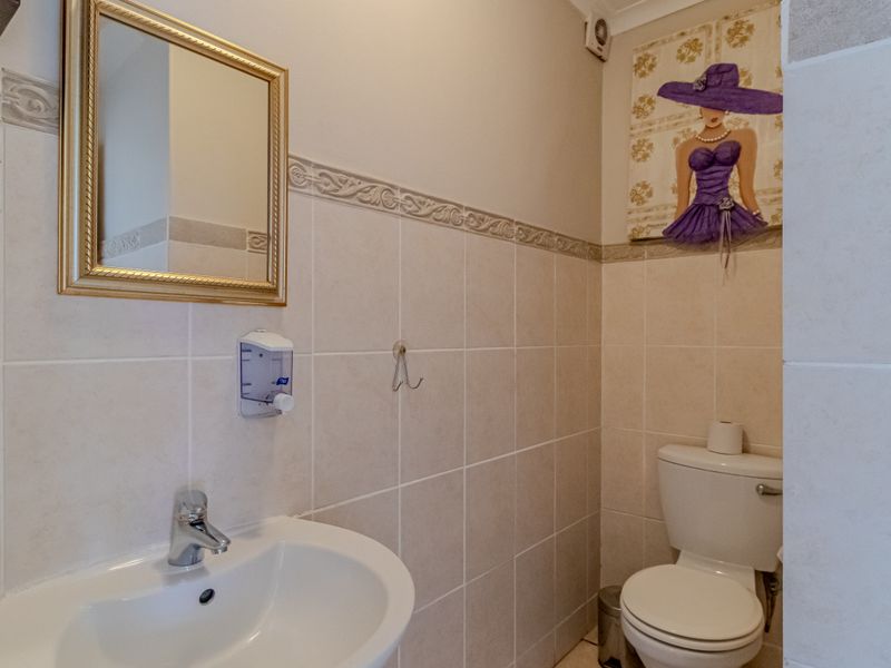 A compact guest bathroom featuring a pedestal basin, chrome mixer tap, and tiled walls with a decorative border.