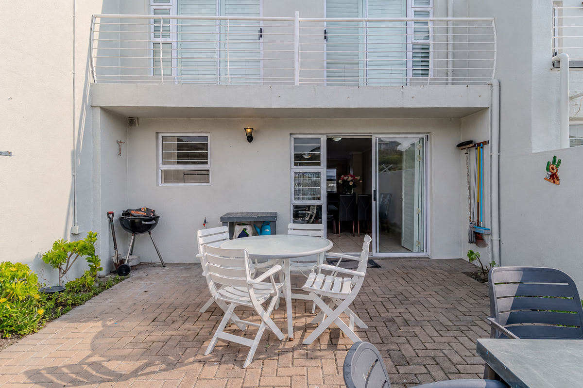 Rear exterior view of the townhouse featuring a paved patio area, sliding door access to the interior, and an upper-level balcony with metal railing.