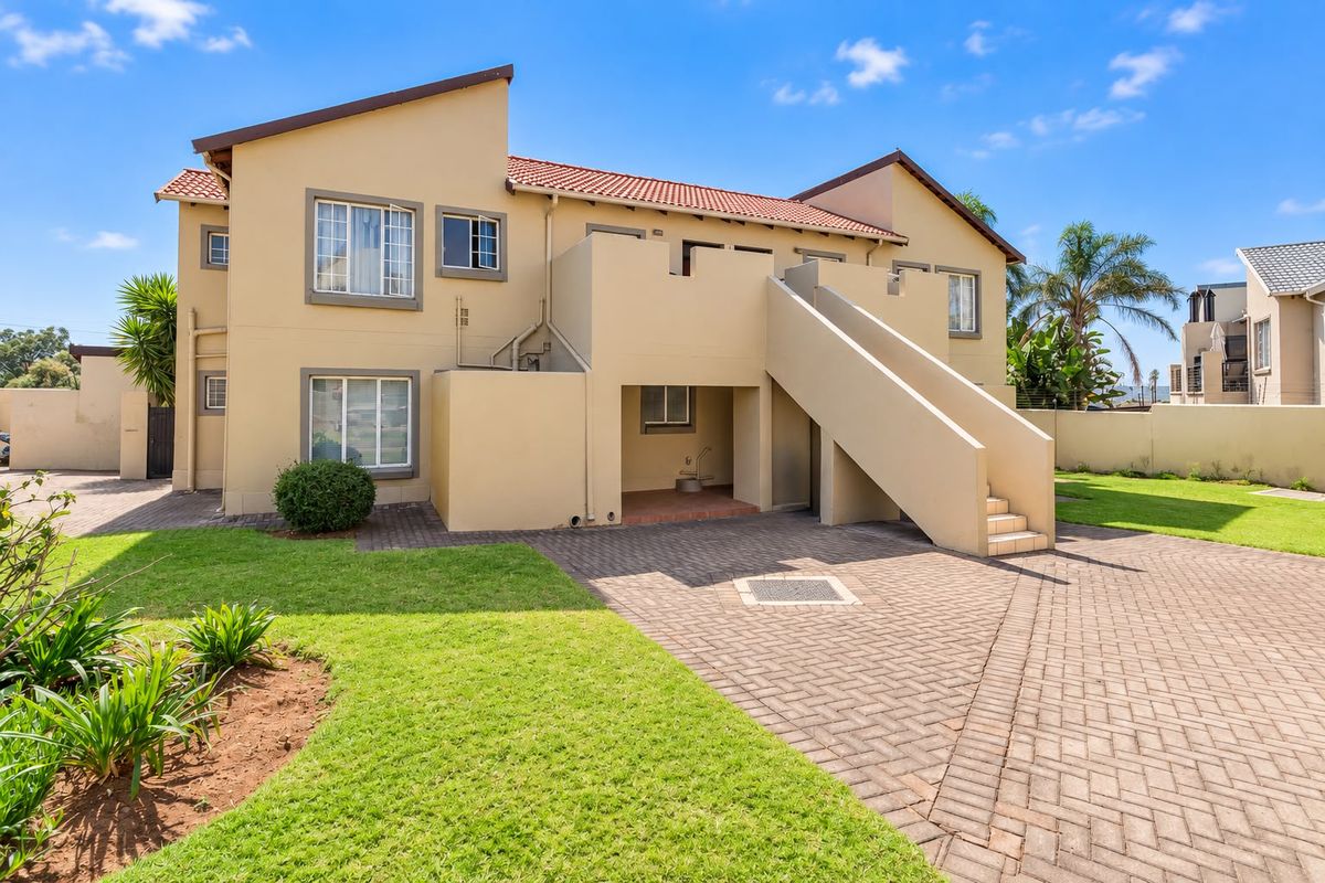 Rear view of the apartment building featuring a paved driveway, external staircase, and well-maintained lawn area.