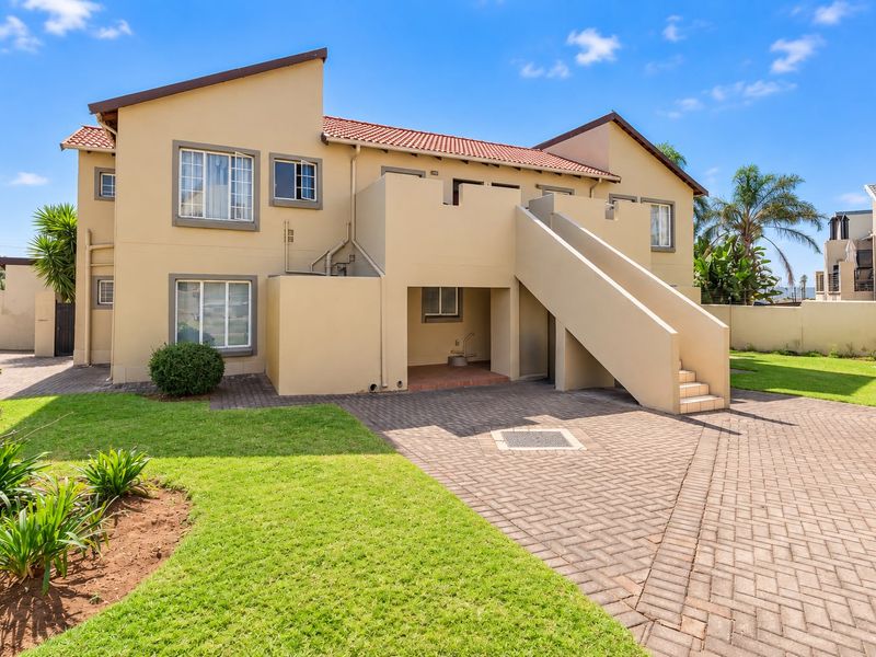 Rear view of the apartment building featuring a paved driveway, external staircase, and well-maintained lawn area.