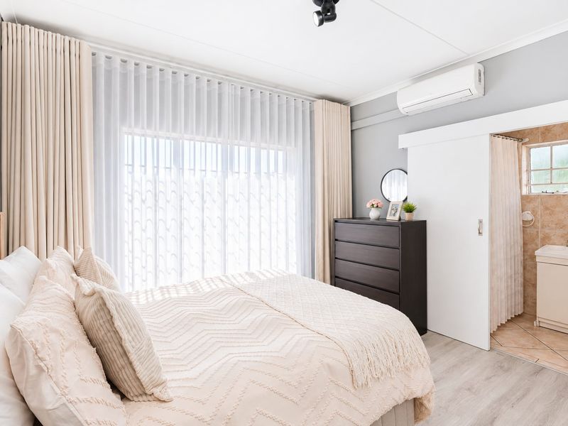 A well-maintained bedroom featuring laminate flooring, an air conditioning unit, and an adjoining en-suite bathroom with a vanity basin.