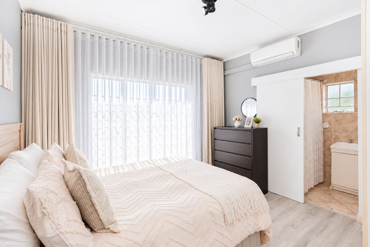 A well-maintained bedroom featuring laminate flooring, an air conditioning unit, and an adjoining en-suite bathroom with a vanity basin.