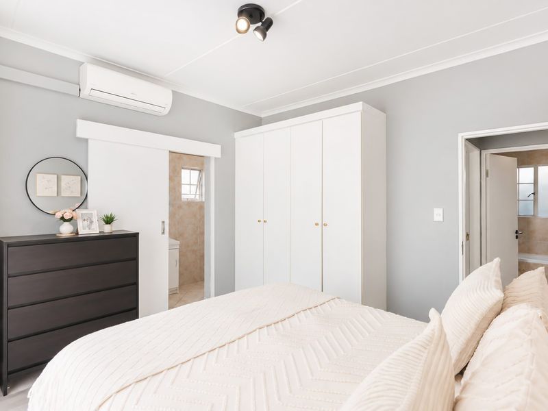A well-maintained bedroom featuring built-in wardrobes, an air conditioning unit, and direct access to an en-suite bathroom.