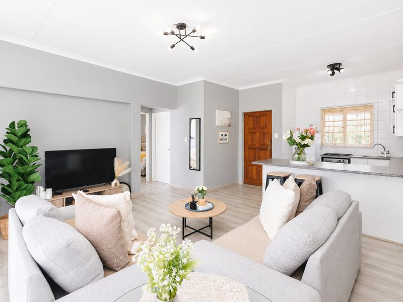Open-plan living area featuring a modern kitchen with breakfast bar, laminate flooring, and neutral wall finishes, creating a bright and functional living space.