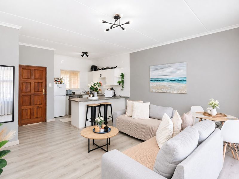 A bright open-plan living and kitchen area featuring modern laminate flooring, neutral grey walls, and a functional kitchen island with breakfast bar seating.