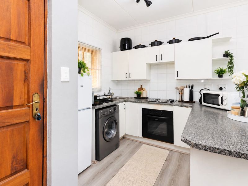 A compact, functional kitchen featuring white cabinetry, granite countertops, a built-in oven, hob, and integrated laundry plumbing.