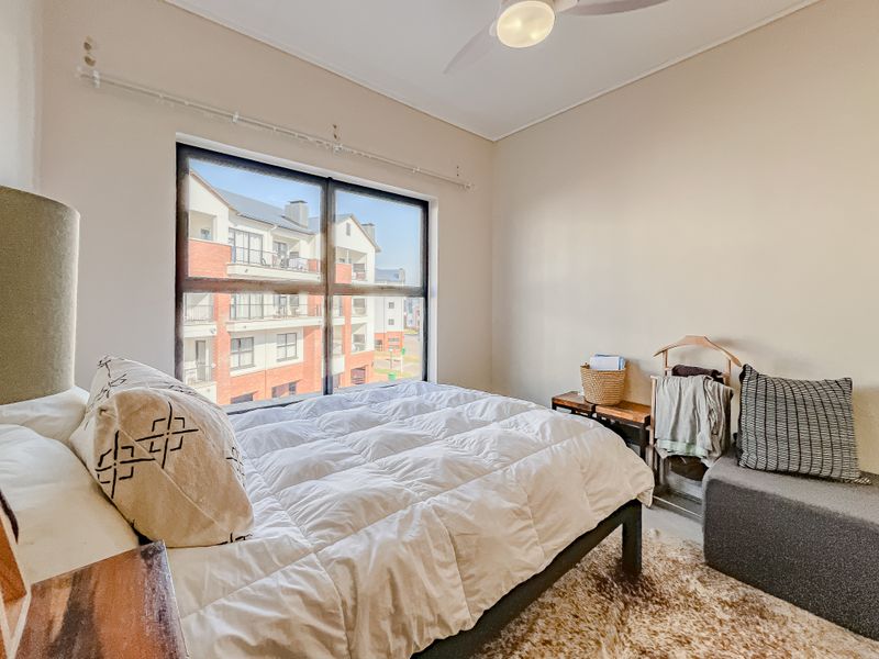 A bright bedroom featuring a large window with natural light and a ceiling fan, offering a comfortable and well-maintained living space.