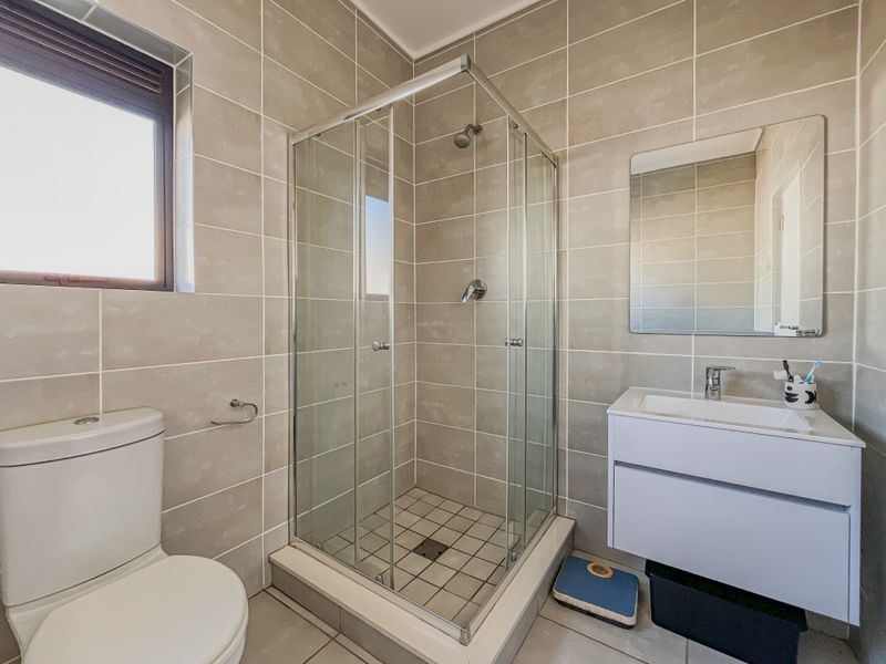 A modern bathroom featuring a glass-enclosed shower, wall-mounted vanity with basin, and neutral ceramic tiling throughout.