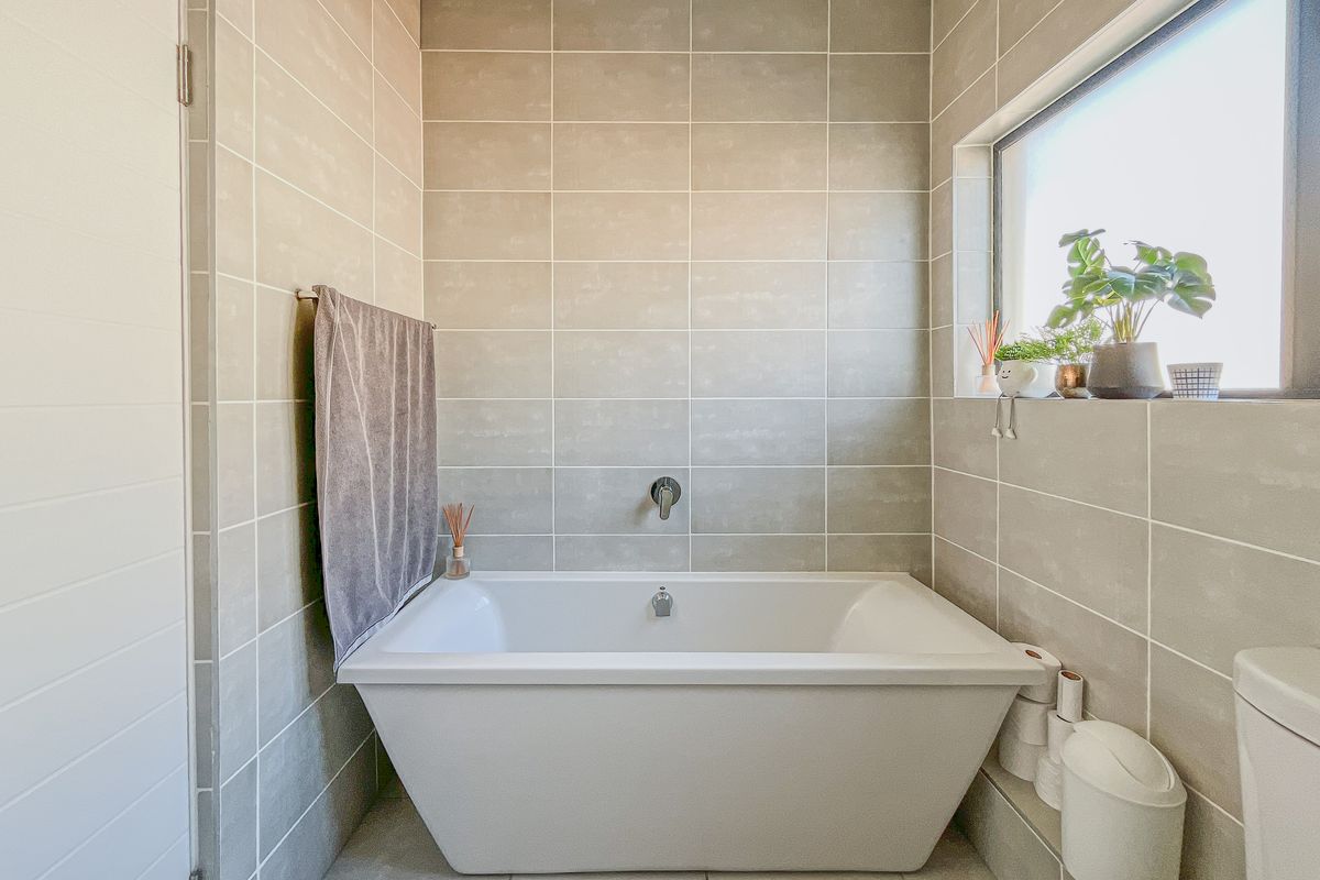 Modern bathroom featuring a sleek freestanding bathtub, neutral ceramic wall and floor tiling, and a window providing natural light.