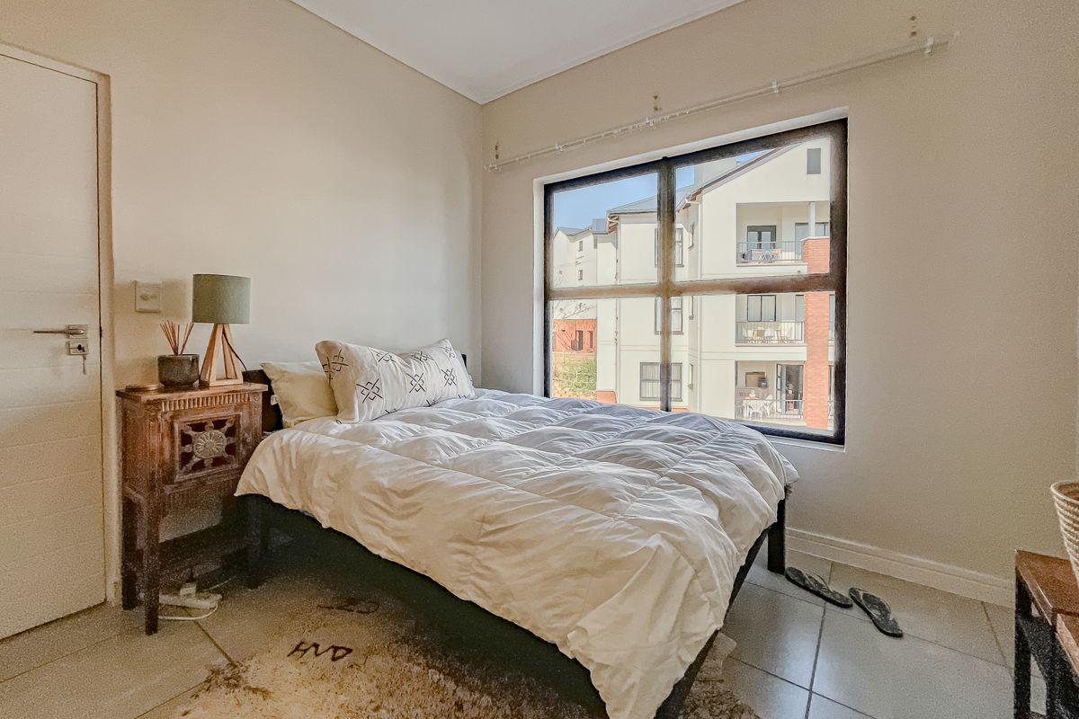 A functional bedroom featuring tiled flooring and a large window that provides natural light and views of the surrounding apartment complex.