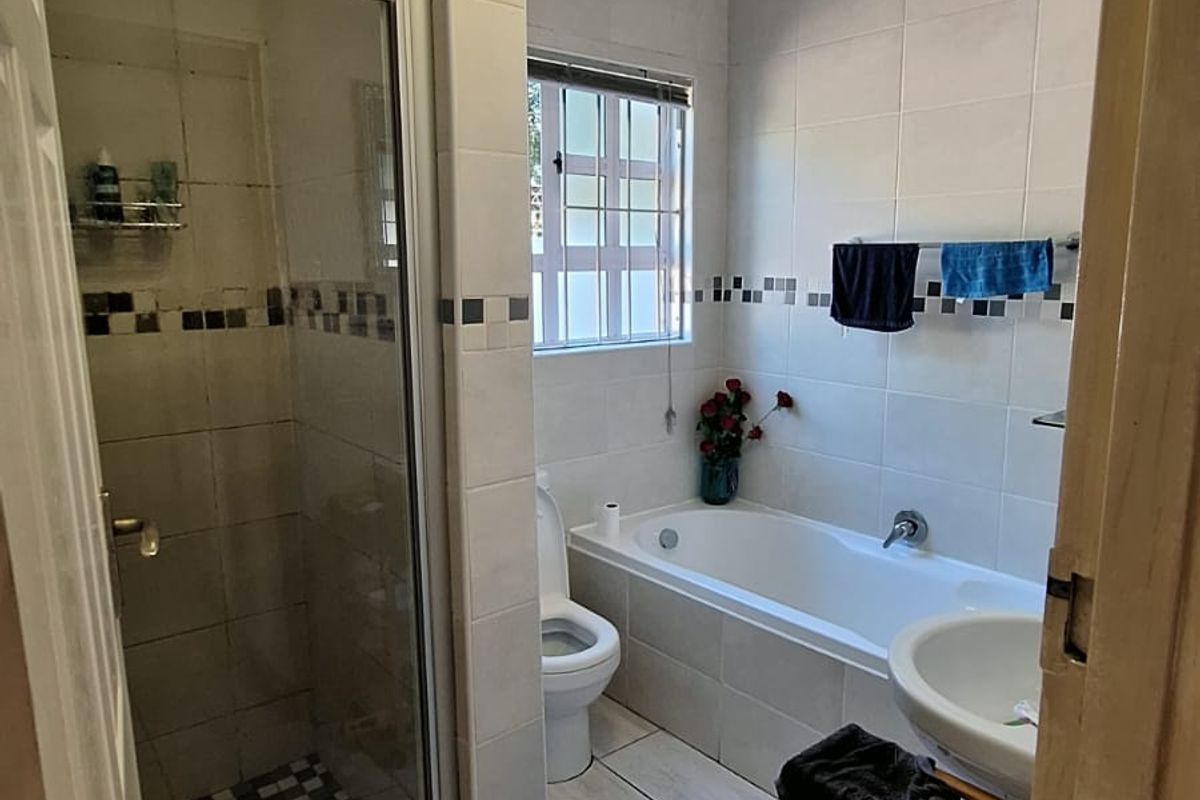 A functional bathroom featuring a separate shower, bathtub, toilet, and pedestal basin, currently showing signs of ceiling water damage requiring maintenance.