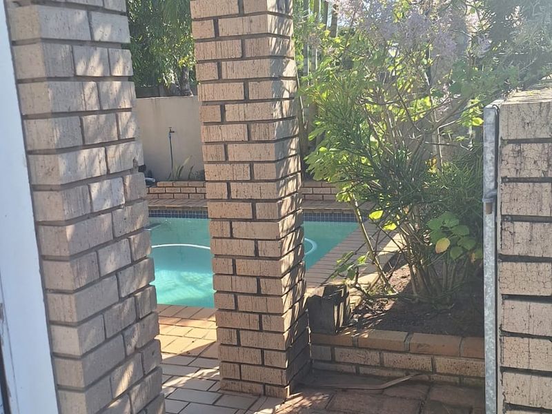 A view of a swimming pool area framed by brick pillars and paved pathways, featuring established garden landscaping.
