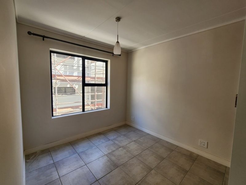 A clean, empty bedroom featuring neutral wall tones, tiled flooring, and a large window with a black aluminium frame.