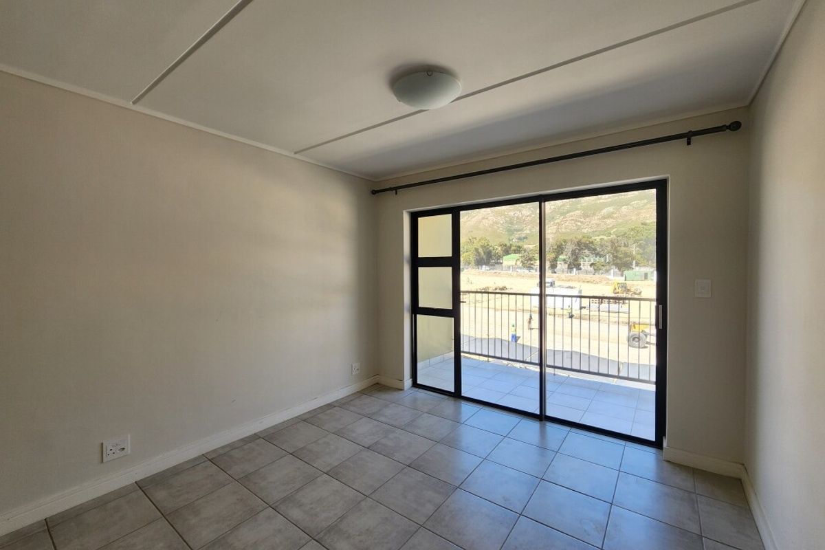 A bright, empty bedroom featuring neutral tiled flooring and a large sliding glass door that opens onto a private balcony with mountain views.