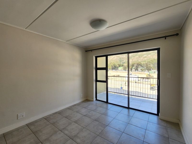 A bright, empty bedroom featuring neutral tiled flooring and a large sliding glass door that opens onto a private balcony with mountain views.