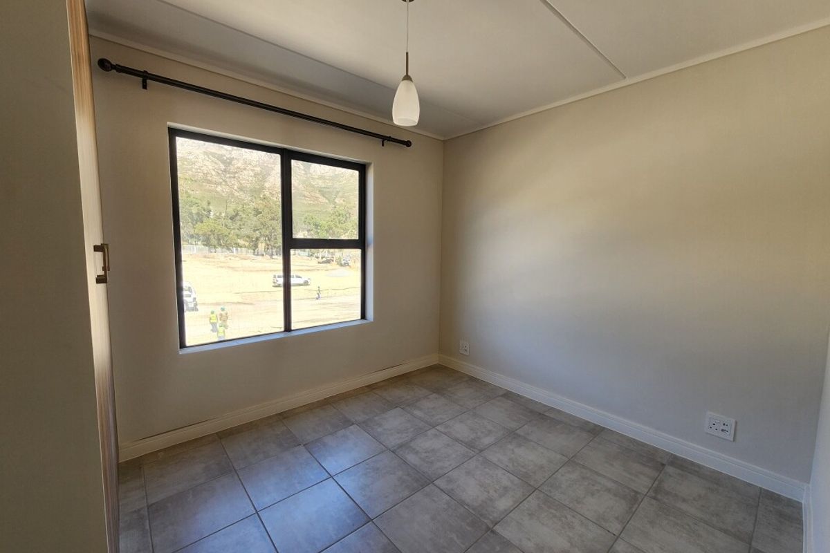 A clean, empty bedroom featuring neutral tiled flooring, a modern pendant light, and a large window with views of the surrounding area.