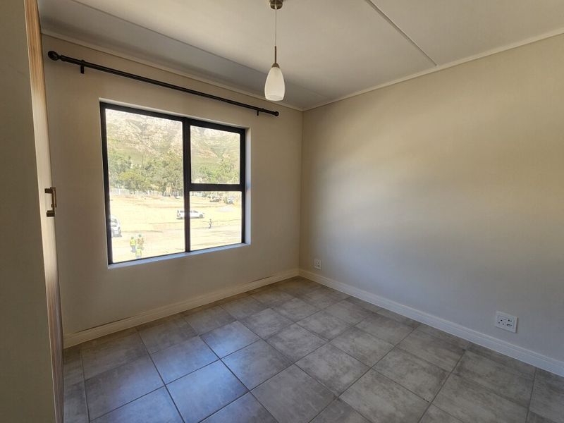 A clean, empty bedroom featuring neutral tiled flooring, a modern pendant light, and a large window with views of the surrounding area.