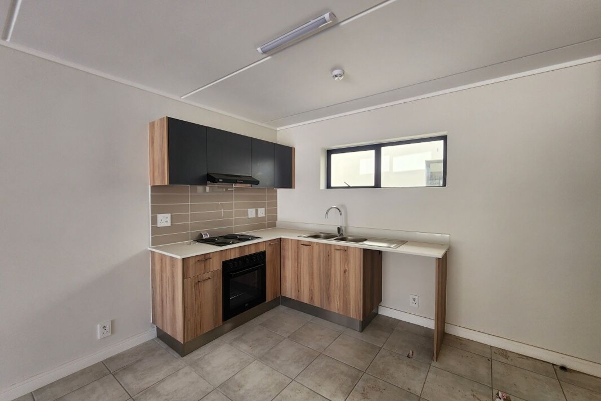 A compact, modern kitchen featuring wood-finish cabinetry, dark upper cupboards, built-in oven and hob, and tiled flooring in a clean, empty space.