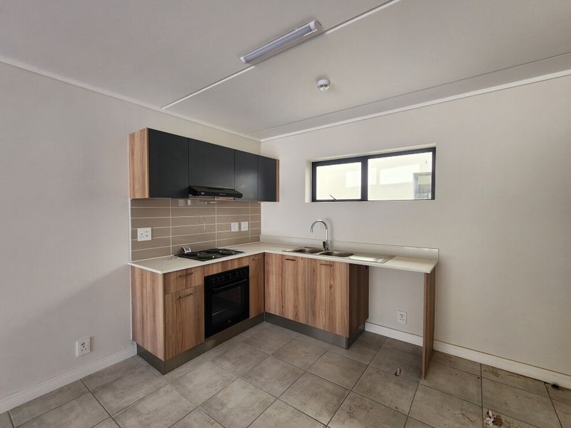 A compact, modern kitchen featuring wood-finish cabinetry, dark upper cupboards, built-in oven and hob, and tiled flooring in a clean, empty space.