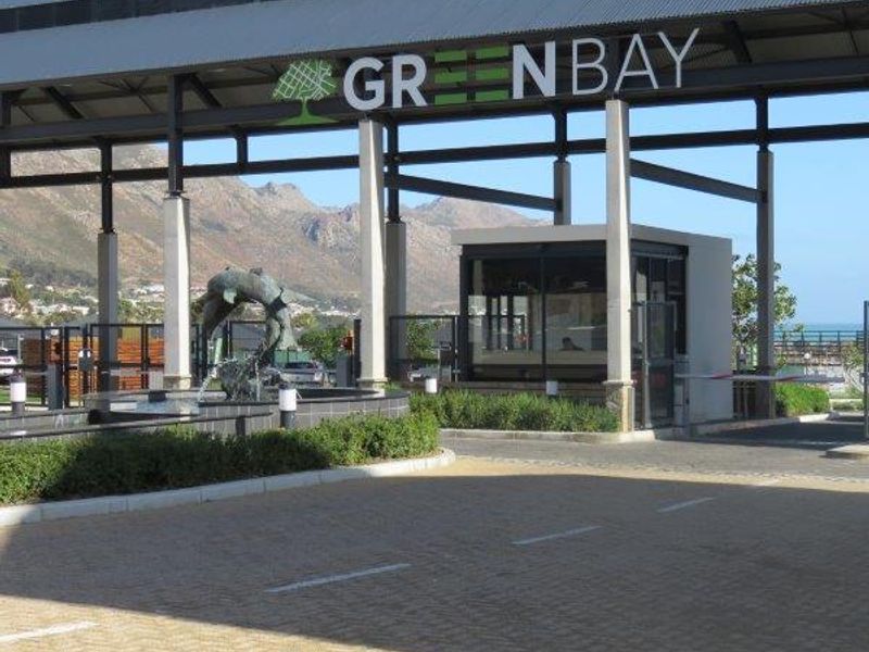 The main entrance and security gatehouse of the Greenbay estate, featuring a paved driveway, modern metal structure, and a decorative water feature.