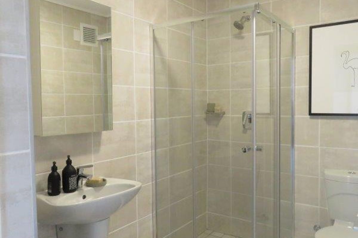 A clean, modern bathroom featuring a glass shower enclosure, wall-mounted basin, and toilet with neutral wall and floor tiling.