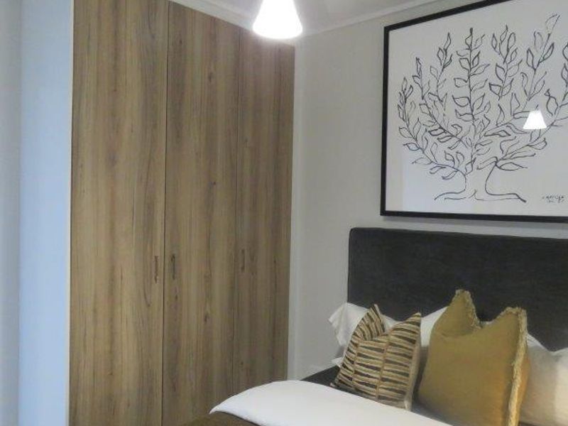 A well-maintained bedroom featuring modern wood-finish built-in wardrobes and a contemporary pendant light fixture.