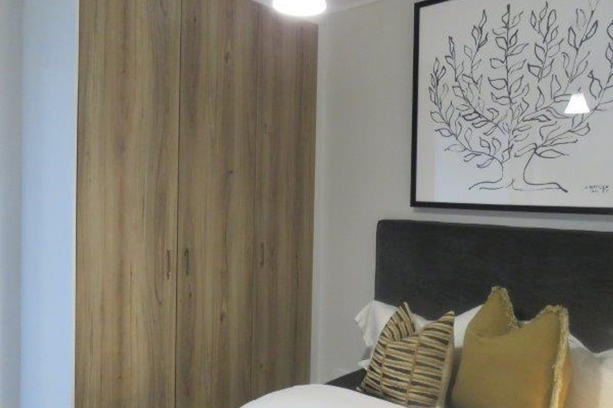 A well-maintained bedroom featuring modern wood-finish built-in wardrobes and a contemporary pendant light fixture.