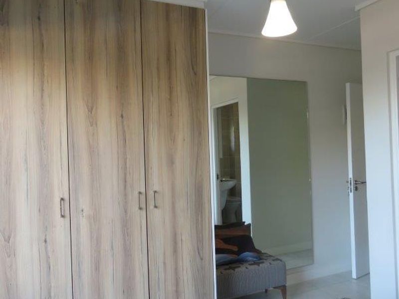 A bedroom featuring modern wood-finish built-in cupboards, a large wall-mounted mirror, and a contemporary pendant light fixture.