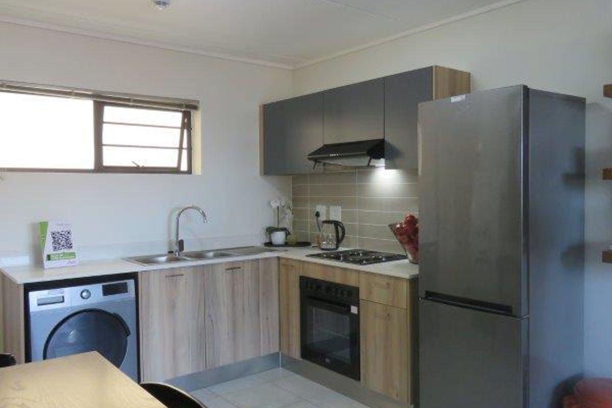 A functional kitchen featuring modern wood-finish cabinetry, a built-in oven with gas hob, extractor fan, and integrated laundry plumbing.
