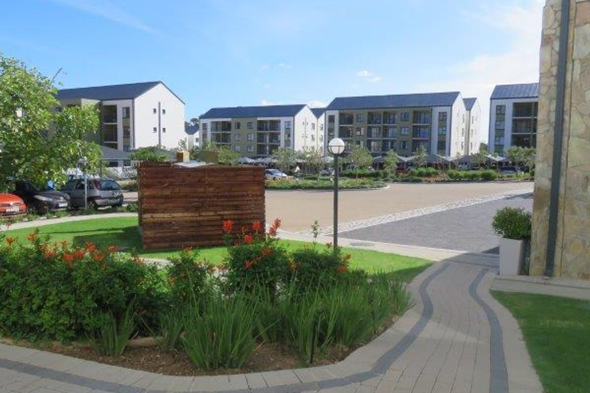 A well-maintained communal garden area featuring paved walkways, stone-clad building accents, and landscaped greenery within an apartment complex.
