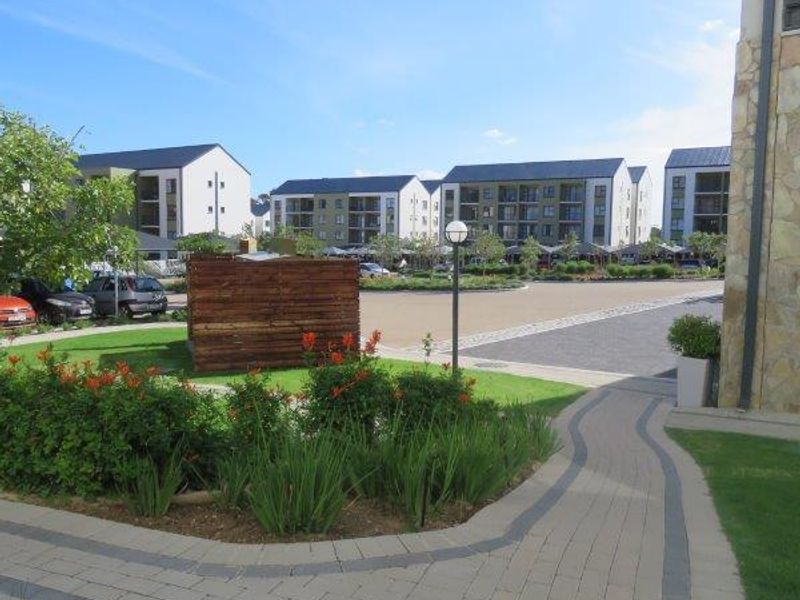 A well-maintained communal garden area featuring paved walkways, stone-clad building accents, and landscaped greenery within an apartment complex.