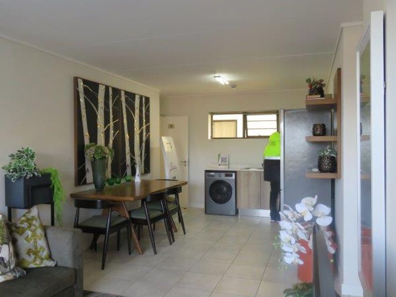 Open plan living and dining area featuring tiled flooring and a compact kitchen corner with built-in cabinetry and laundry plumbing.
