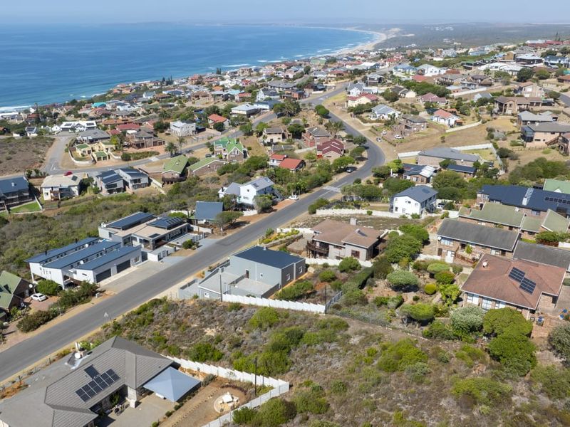 An aerial view of a coastal residential neighborhood showing the surrounding landscape, street layout, and available vacant land plots.