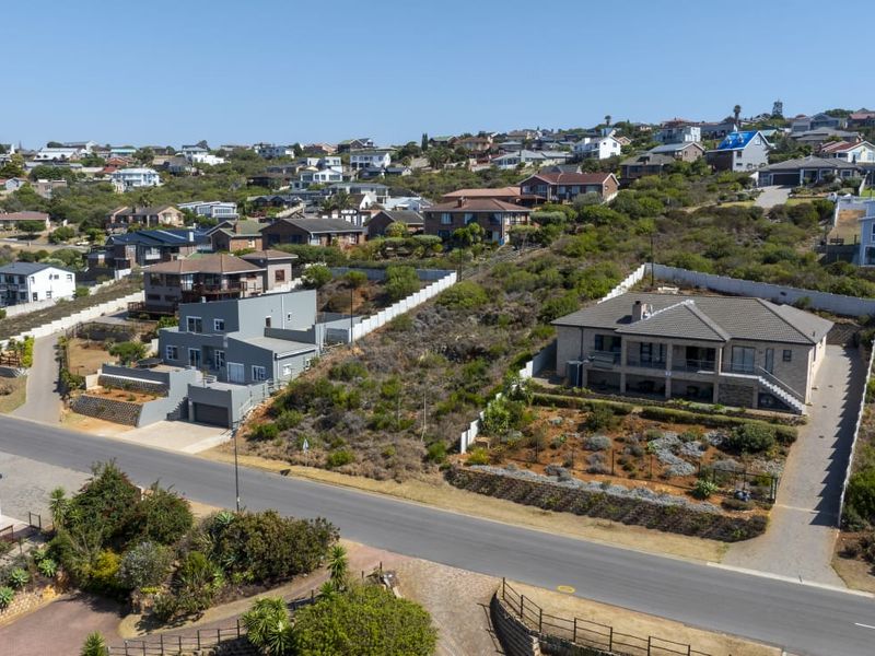 An aerial view of a residential neighborhood featuring vacant land plots, paved roads, and established surrounding homes in a coastal hillside setting.