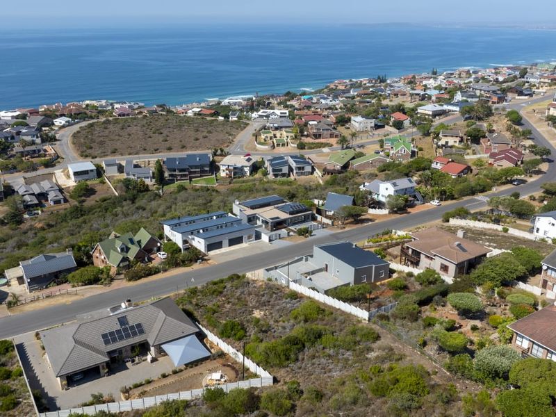 An elevated aerial view of a coastal residential neighborhood, showcasing the surrounding landscape, street layout, and proximity to the ocean.