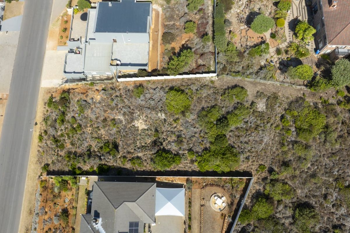An aerial view of a vacant residential plot situated between existing properties, featuring natural vegetation and established boundary fencing.