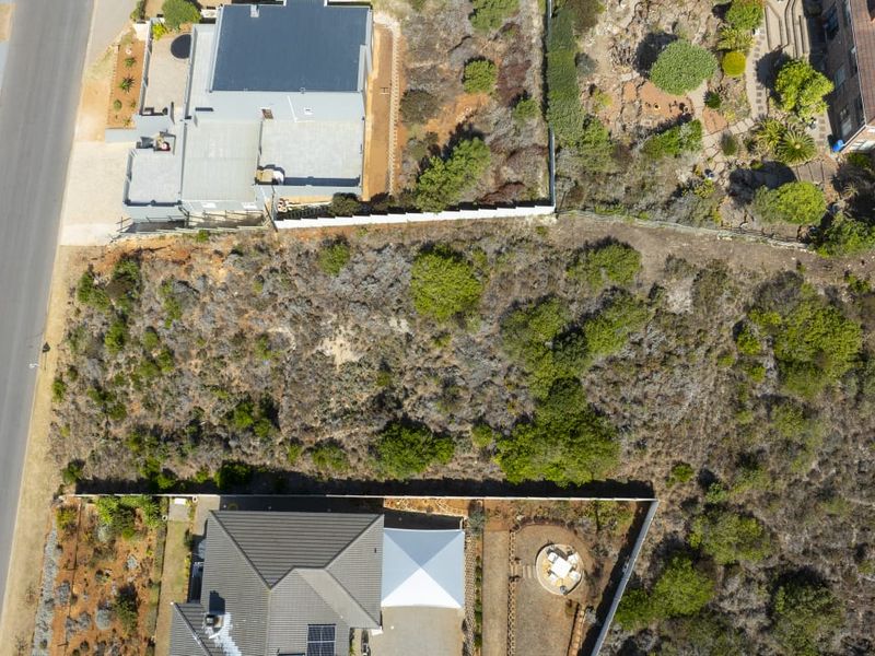 An aerial view of a vacant residential plot situated between existing properties, featuring natural vegetation and established boundary fencing.
