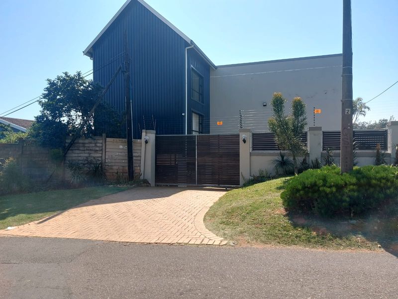 Front exterior view of the property featuring a paved driveway, secure electric gate, and modern metal cladding on the building facade.