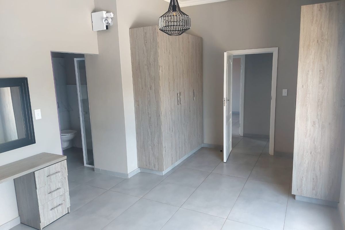Spacious bedroom featuring neutral tiled flooring, built-in cupboards, and an en-suite bathroom, offering a clean and modern living space.