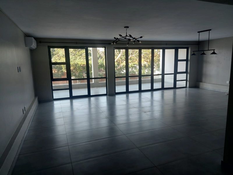 Spacious, empty living area featuring large format floor tiles, modern pendant lighting, and expansive black aluminium sliding doors leading to an outdoor space.